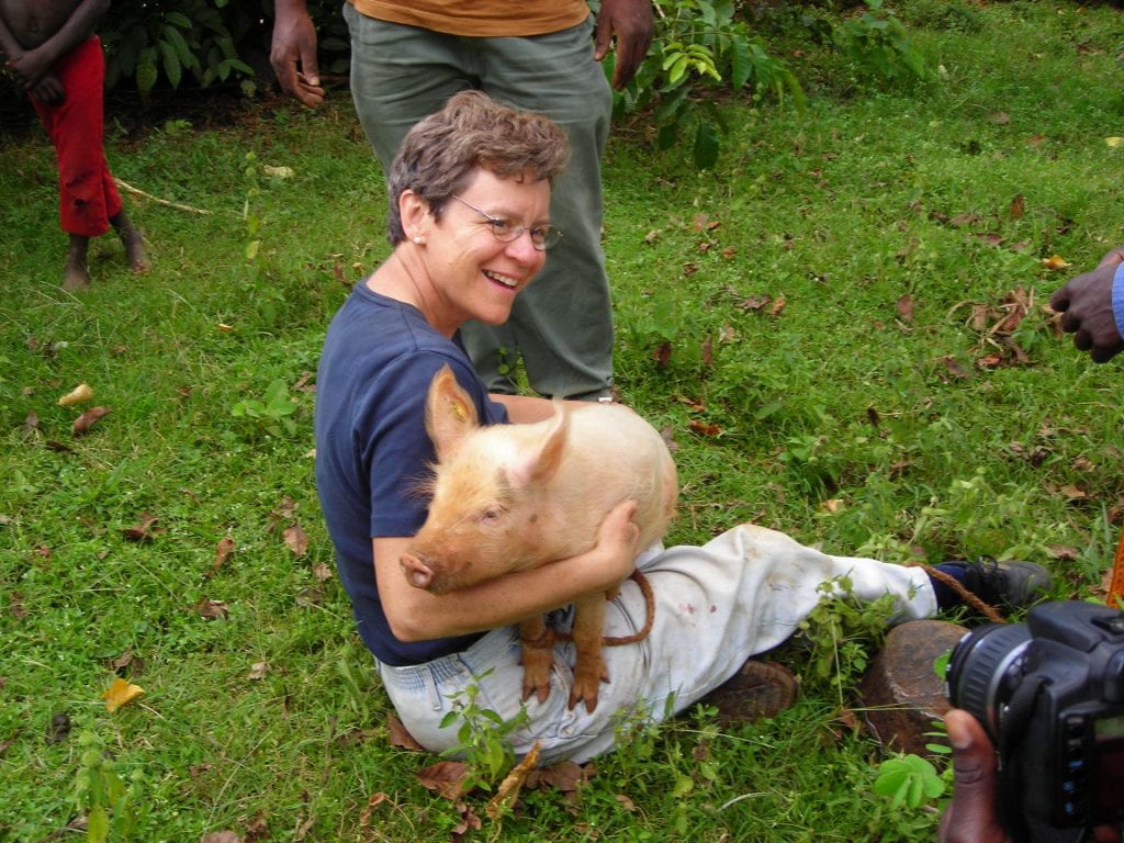 Image of Cate Dewey in Kenya sitting in the grass while holding a pig.