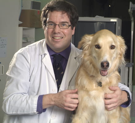 Photo of Dr. Paul Woods in a lab coat standing beside a Golden Retriever dog.