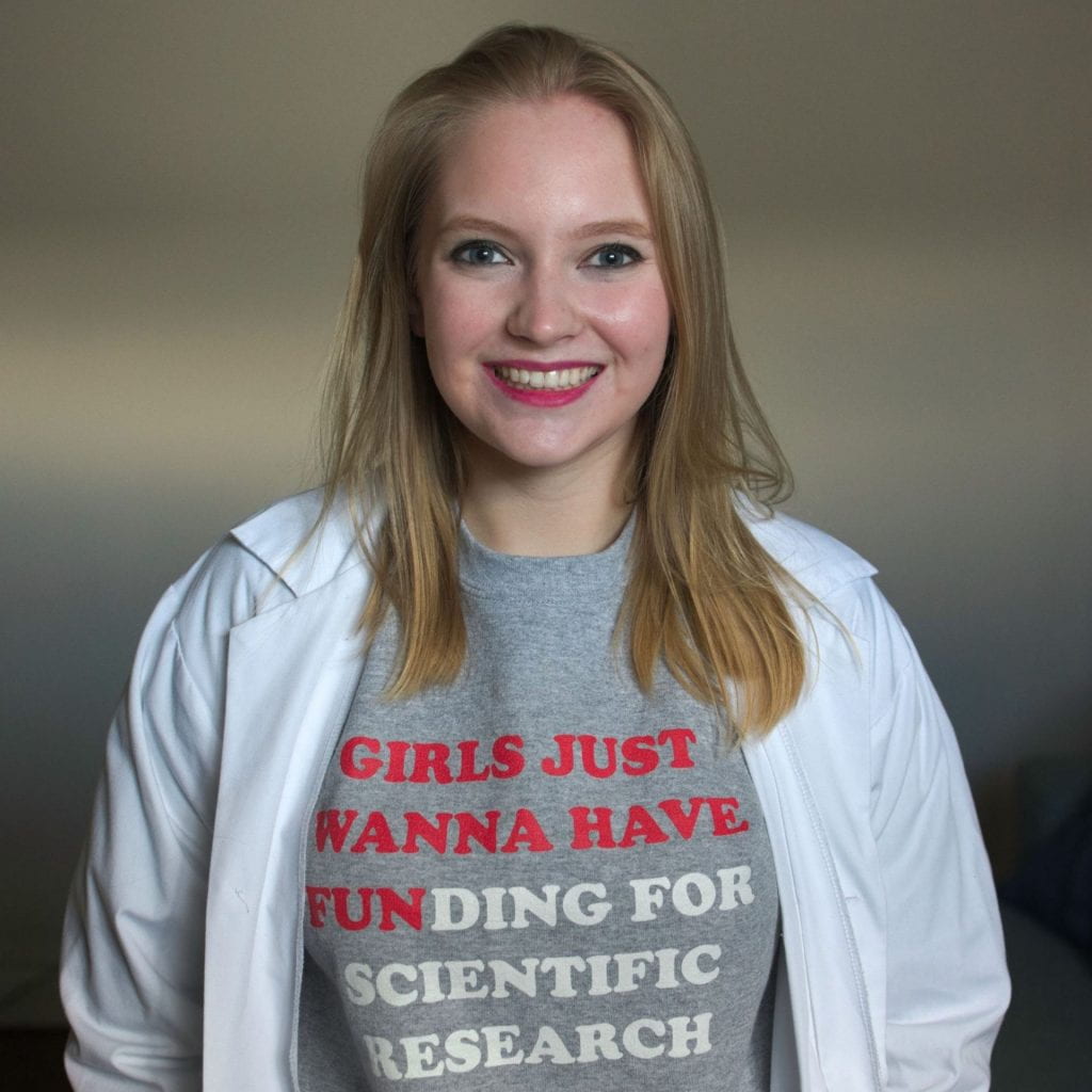 Headshot of Nikola May wearing a shirt that says "Girls just wanna have funding for scientific research"